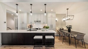 A modern kitchen with a central island, pendant lighting, and a dining area with a long table and chairs.