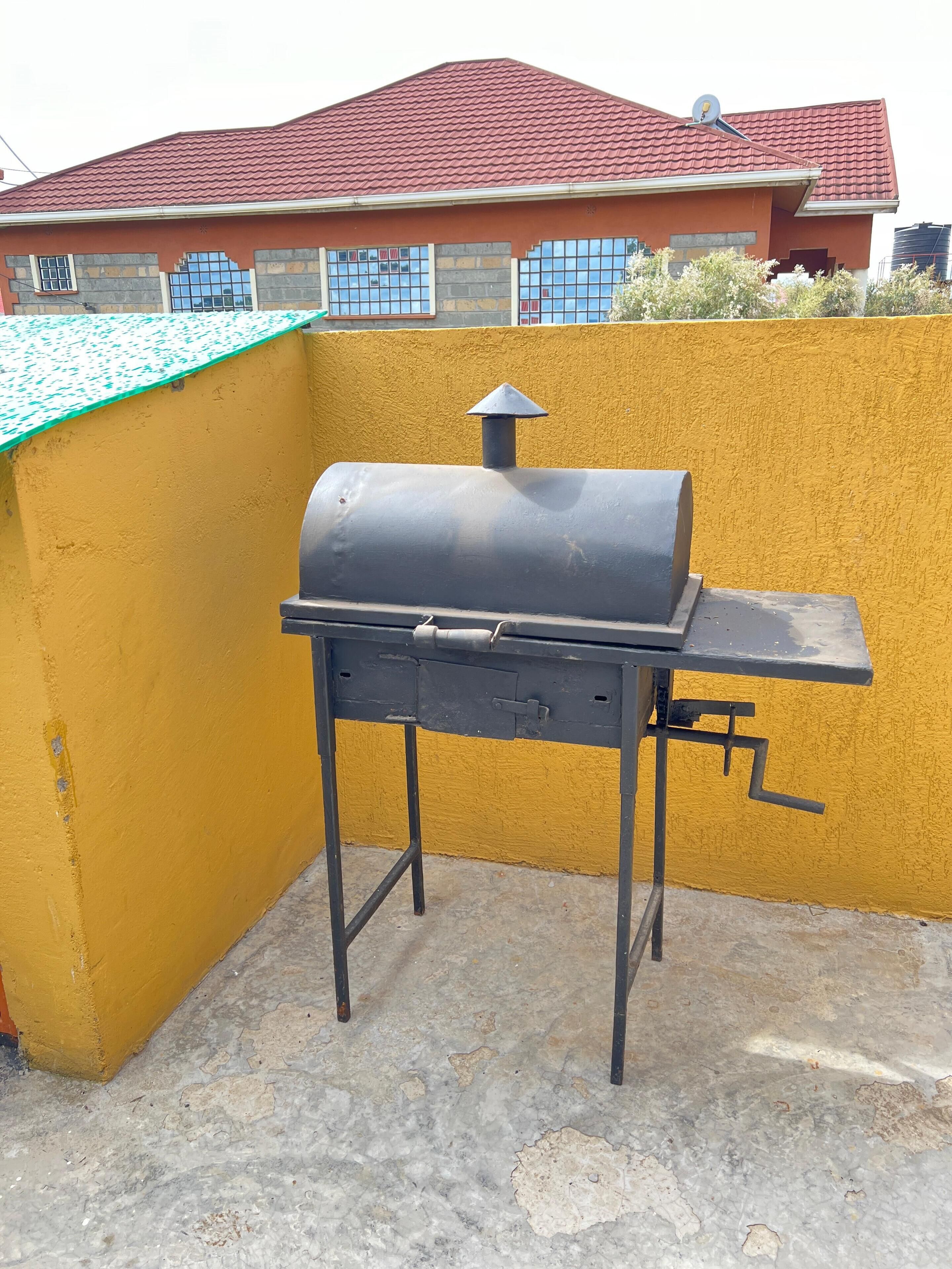 A barbecue grill on a rooftop with a yellow wall and a red-roofed building in the background.