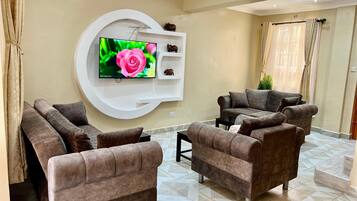 Una sala de estar moderna con un televisor de pantalla plana grande montado en una pared blanca, un sofá marrón y un suelo estampado.