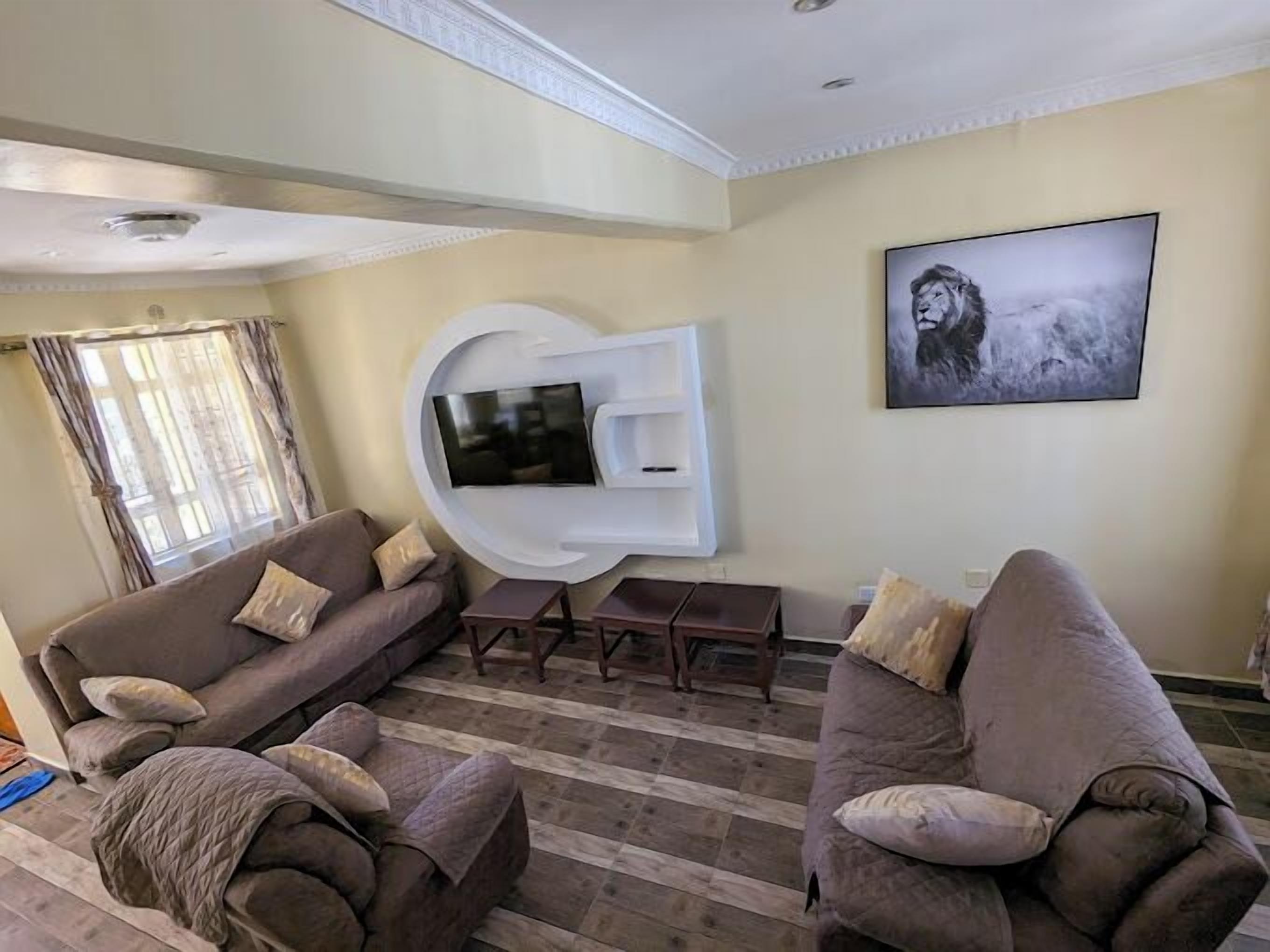 A living room with two sofas, a TV mounted on a white wall, a window with curtains, and a painting on the wall.