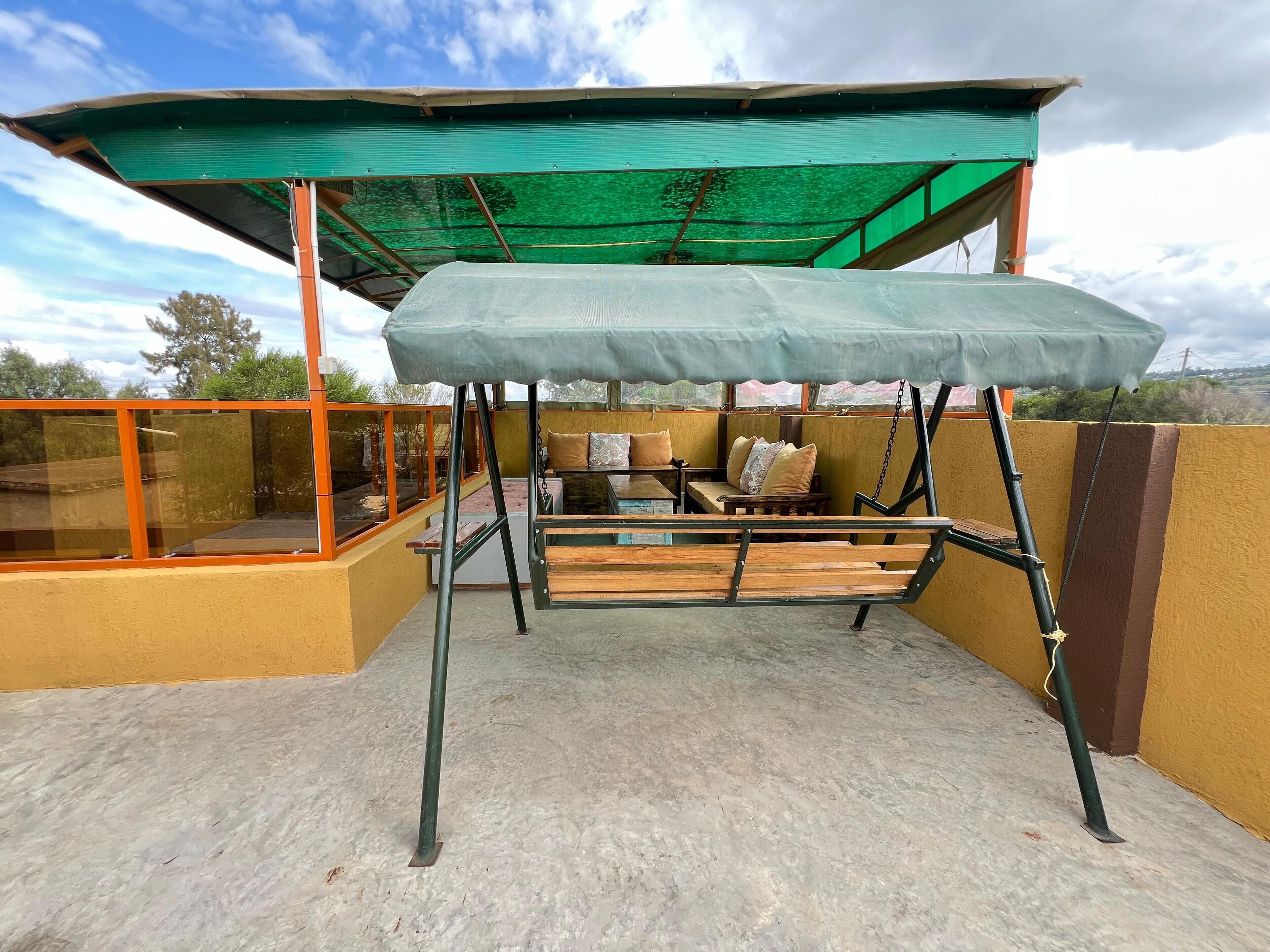 Un espacio al aire libre techado con una silla colgante, bancos de madera y asientos acolchados.