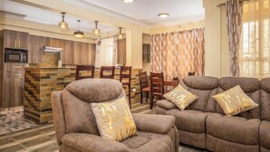A living room with a sofa set and a dining area with chairs and a table. - Lux Suites Sunset Delight Holiday Homes (Naivasha)