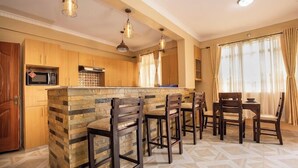A kitchen with a stone island, wooden cabinets, and bar stools. - Lux Suites Sunset Delight Holiday Homes (Naivasha)