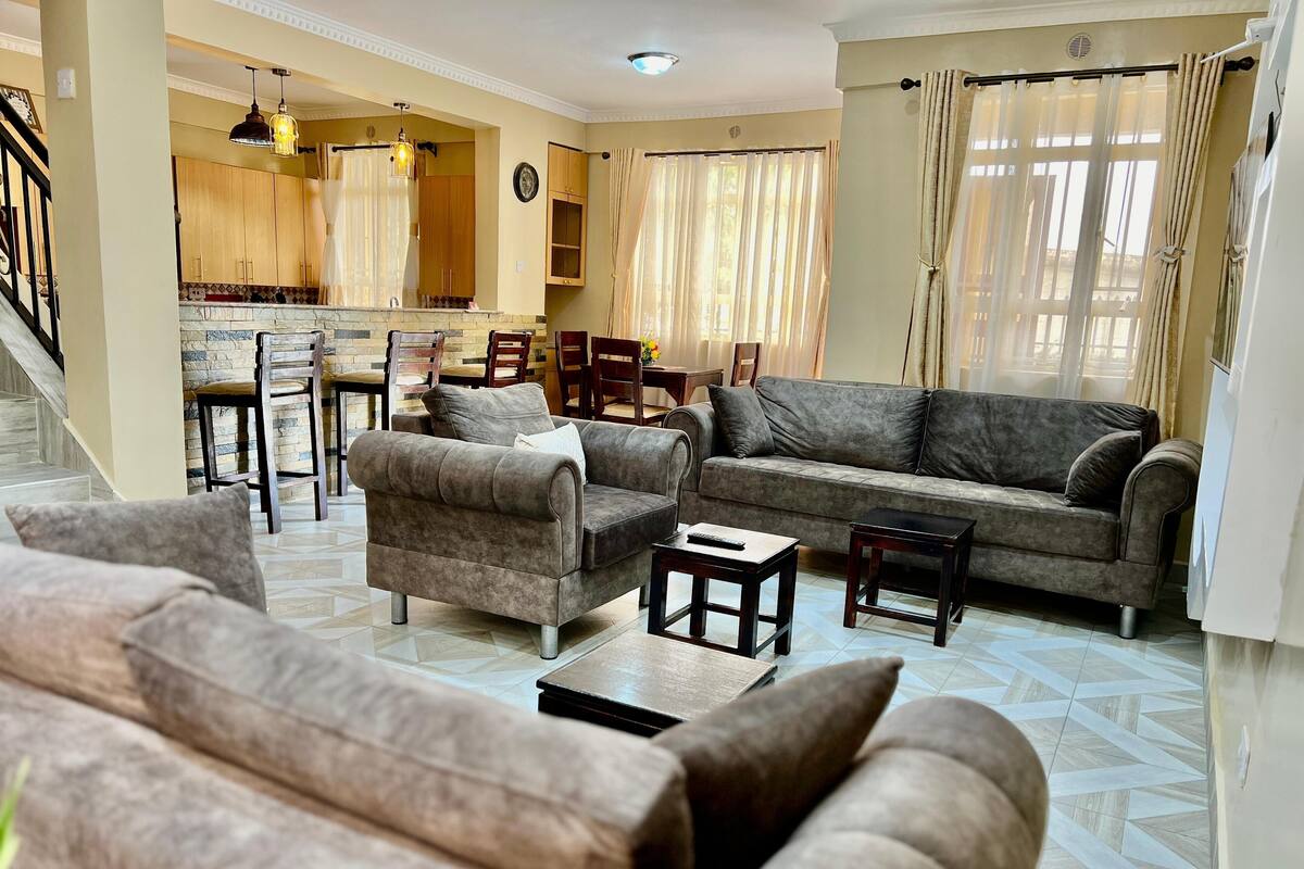 A living room with a sofa, armchairs, and a coffee table. There is a staircase leading to an upper level.