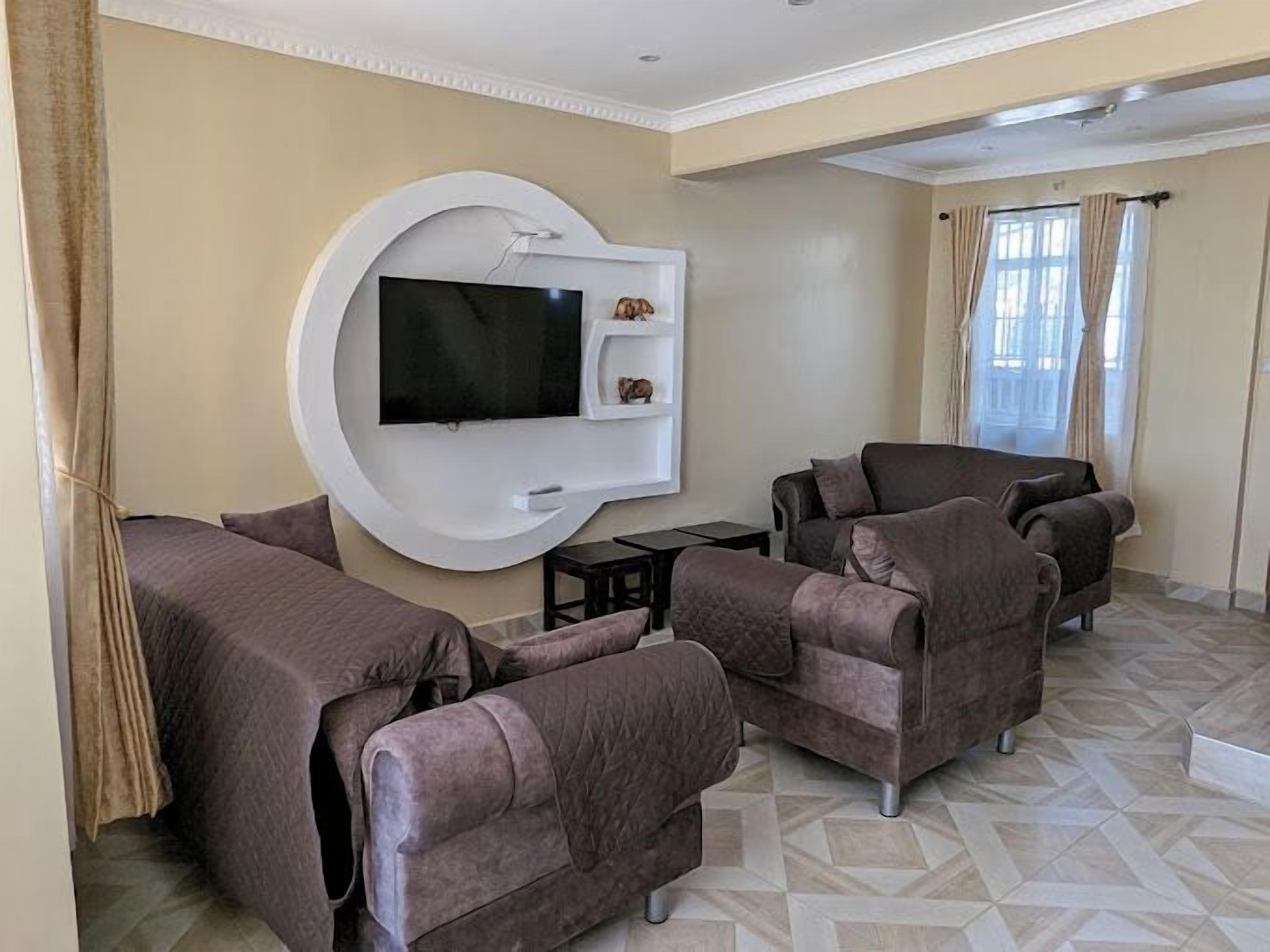 Una sala de estar moderna con un televisor grande montado en una pared blanca, rodeada de sillones cómodos y una pequeña mesa de centro.