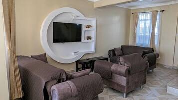 Una sala de estar moderna con un televisor grande montado en una pared blanca, rodeada de sillones cómodos y una pequeña mesa de centro.