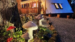 A rustic cabin with string lights, a deck, and mushroom-shaped planters.