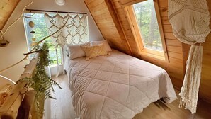 A cozy attic bedroom with a bed, a large window, and a ceiling decoration.