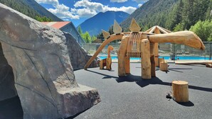 A wooden dinosaur sculpture in a park with a mountain backdrop.