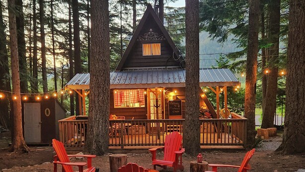 A cabin with a wooden exterior, a deck, and red Adirondack chairs.