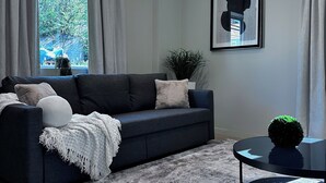 Un salon moderne avec un canapé bleu foncé, une table basse ronde et une grande fenêtre avec des rideaux.