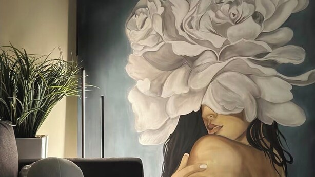 Une pièce avec un grand décor mural représentant des motifs floraux, un canapé, une plante en pot et une lampe.