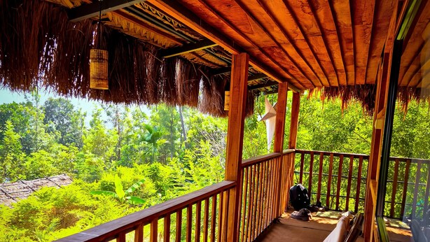 Un balcón de madera con techo de paja, con vistas a un paisaje verde exuberante.