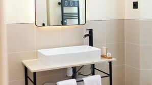 A modern bathroom with a white sink, black faucet, and a mirror above it. There is a towel rack below the sink holding two white towels. - Hotel Tinah: Elegance and Comfort Near the Champs-elysees (Paris)