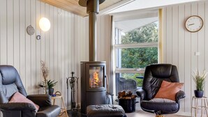 A cozy living room with a wood-burning stove, two leather chairs, a round ottoman, and a large window offering a view of greenery. - "Dorethea" - 30km from the sea by Interhome (Toftlund)