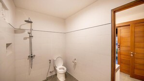 Pieni, siisti kylpyhuone, jossa on valkoiset laatat, suihku ja wc.