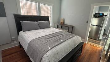 A bedroom with a bed, bedside table, and a view into the kitchen.