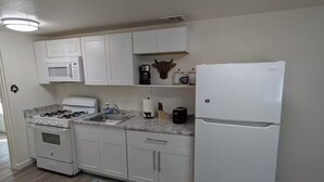 A modern kitchen with white cabinets, a gas stove, a microwave, a coffee maker, and a refrigerator.