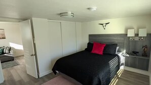 A bedroom with a bed, a pink rug, a white wardrobe, and a headboard with a skull decoration.