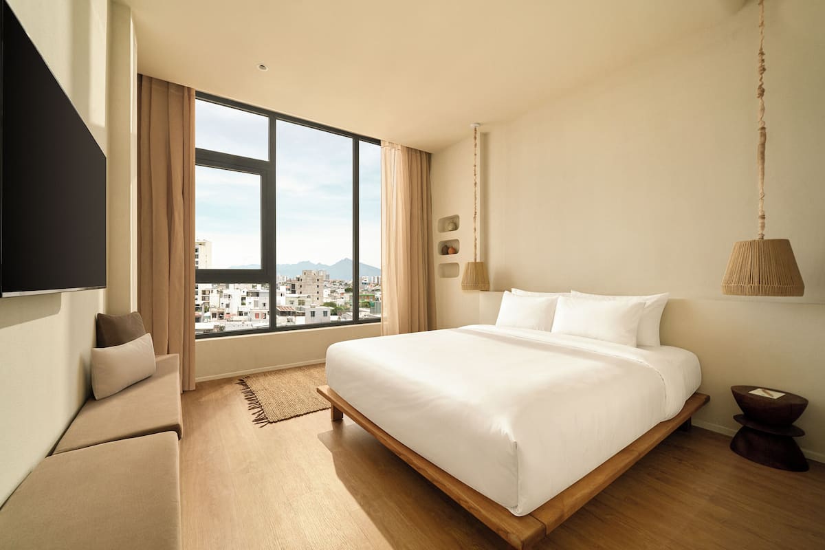 A modern hotel room with a large bed, a sofa, a TV, and a view of the city.