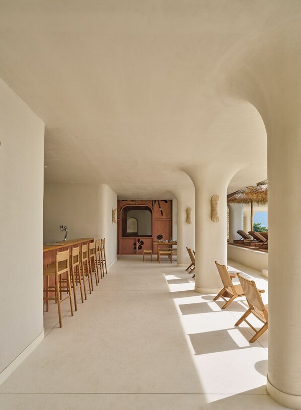 A spacious corridor with a long wooden table and chairs, leading to a kitchen area with a large window.