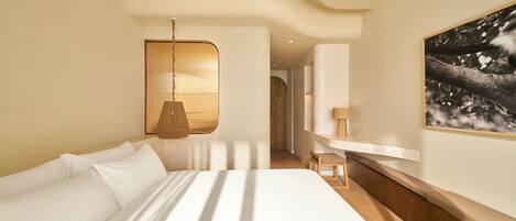 A modern hotel room with a large bed, a wooden bench, a hanging lamp, and a framed picture on the wall.