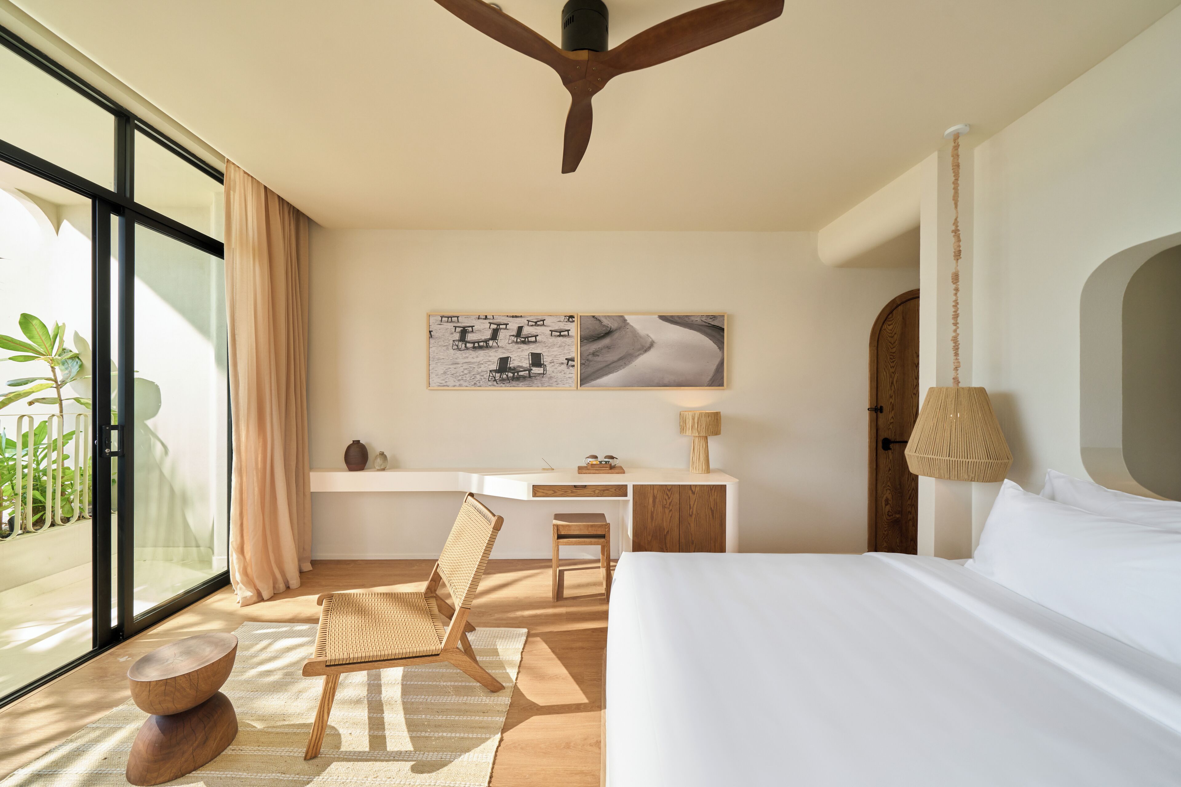 Ein modernes Hotelzimmer mit einem großen Bett, einem Schreibtisch, einem Sessel und Blick ins Freie.