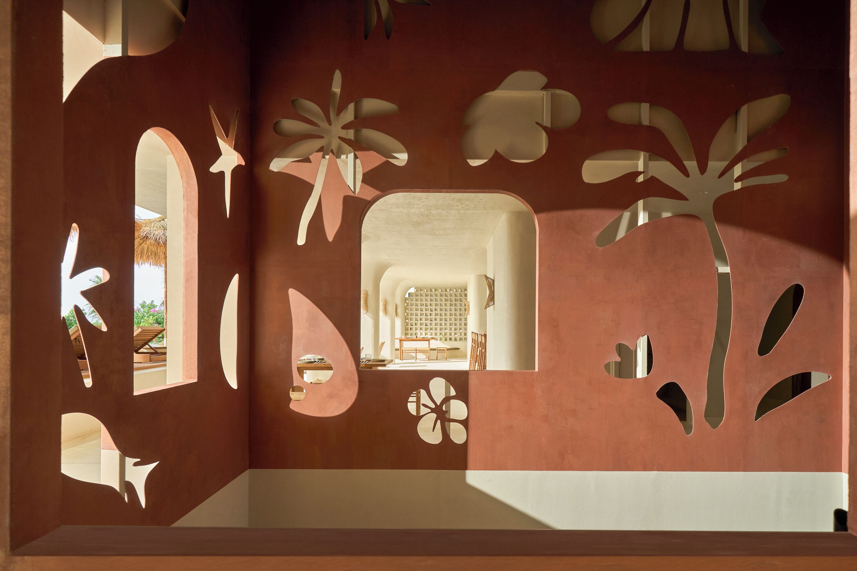A room with a unique wall design featuring cut-out shapes, a central seating area, and a view of an outdoor space.