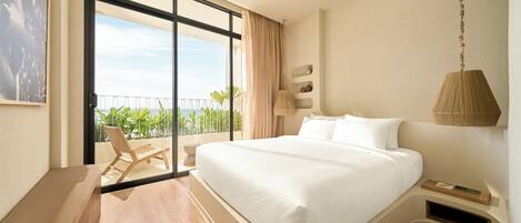 A modern hotel room with a large bed, a balcony with a chair, and a view of greenery.