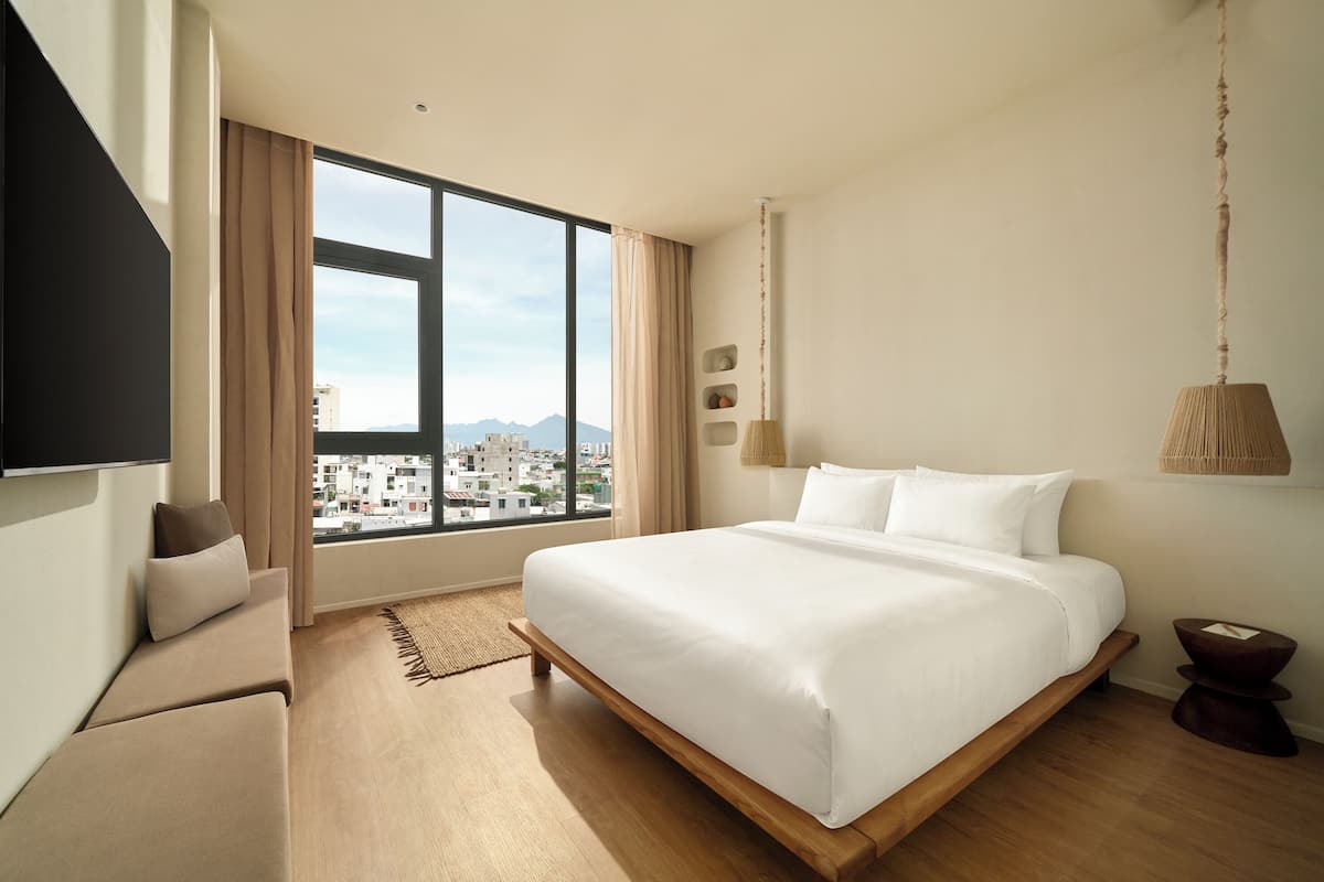 A modern bedroom with a large bed, a sofa, a TV, and a view of a cityscape through a large window.