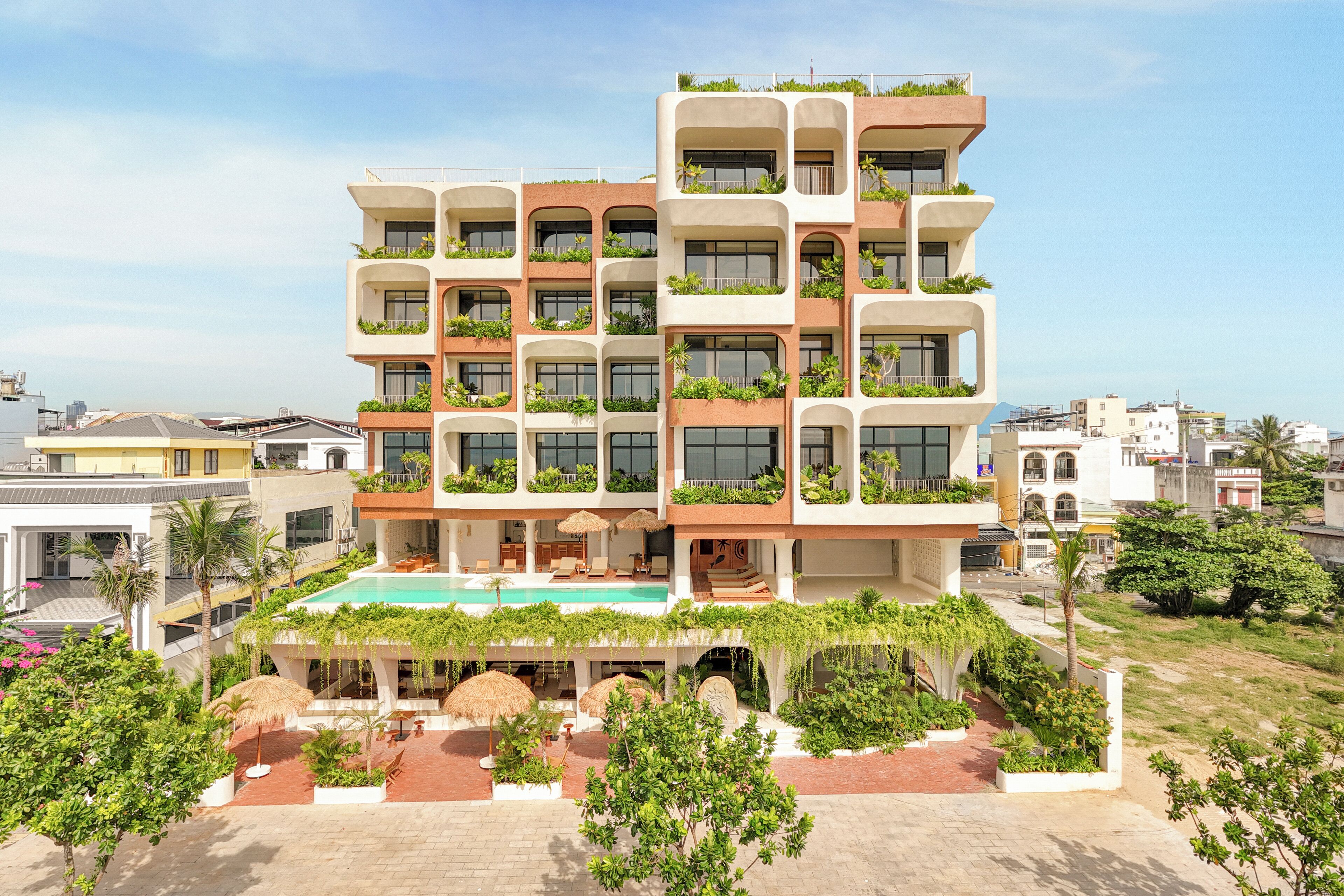 Un hotel de varios pisos con balcones, piscina y abundante vegetación.
