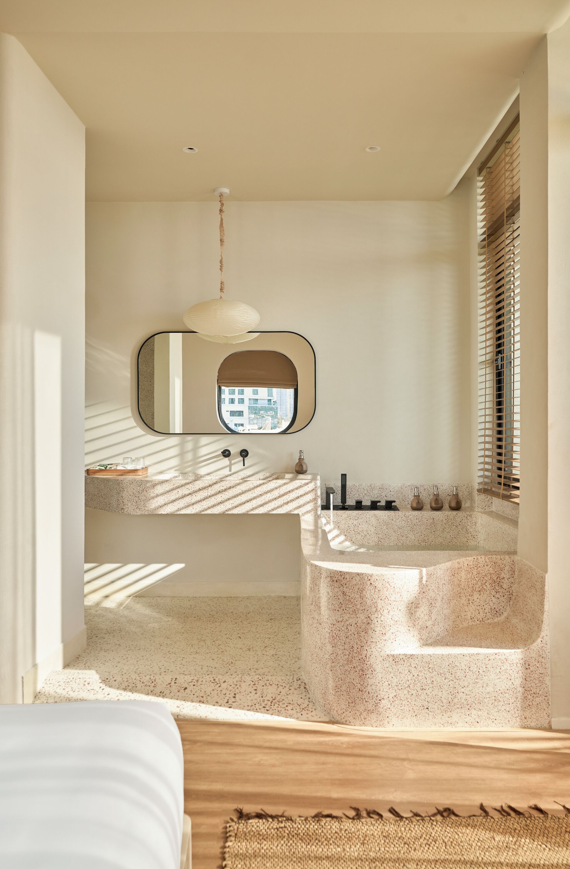 A modern bathroom with a freestanding bathtub, a large mirror, and a window with blinds.
