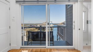 Amplia habitación con piso de madera, puertas correderas de vidrio que dan a una terraza exterior con vista a un puerto deportivo y al agua.