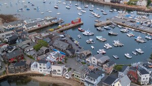 Un pueblo costero con un puerto deportivo lleno de barcos, casas a lo largo de la ribera y un paisaje montañoso al fondo.