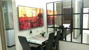 A dining area with a table, chairs, a TV mounted on the wall, and a window with a view.