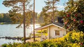 A cabin by a lake with a dock, surrounded by trees and vegetation. - Stay North - Merimaa (Tallbacka)