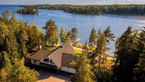 A house with a sloped roof, surrounded by dense trees and a large body of water. - Stay North - Merimaa (Tallbacka)
