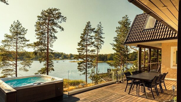 A wooden deck with a hot tub and dining area overlooking a lake. - Stay North - Merimaa (Tallbacka)