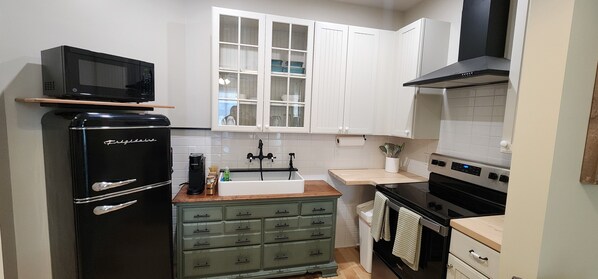 A compact kitchen with a black refrigerator, a microwave, a sink, a stove, and white cabinets.
