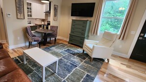 Un salon moderne avec un canapé en cuir marron, une table basse blanche et un coin repas comprenant une table ronde et des chaises. Un téléviseur à écran plat est fixé au mur, au-dessus du coin repas.