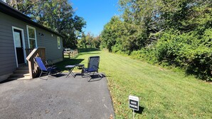 Un espace de stationnement réservé aux visiteurs, avec deux chaises de jardin et une petite table, un panneau d’accueil et une maison dotée d’un porche couvert.
