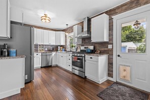 A modern kitchen with white cabinets, a stainless steel refrigerator, a double oven, and a wooden accent wall.
