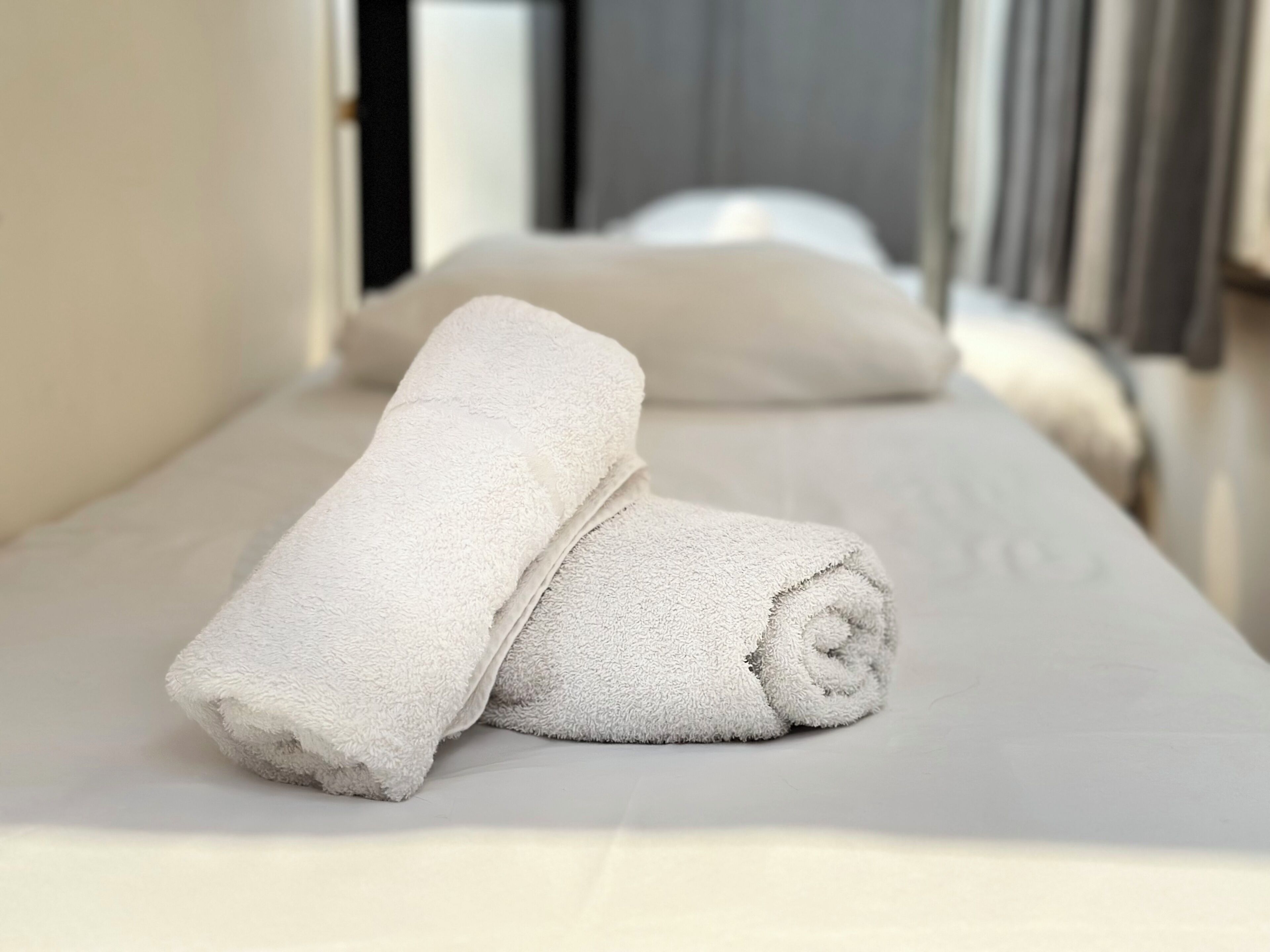 A neatly made bed with two rolled white towels and a pillow.