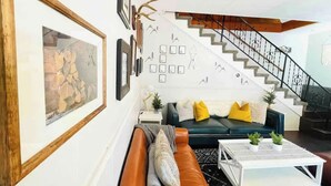 A living room with a staircase, a sofa, a coffee table, and wall art.