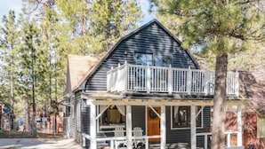 A cabin with a balcony, a porch with chairs, and a wooden door.