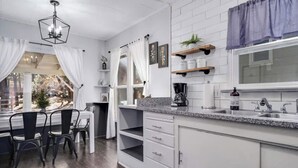A modern kitchen with white cabinetry, a granite countertop, and a window with white curtains.