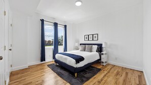 A bedroom with a bed, a nightstand, a window with curtains, and a view of the outside.