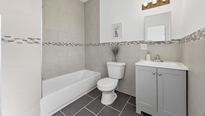 A modern bathroom with a bathtub, toilet, vanity, and a mirror with lights.