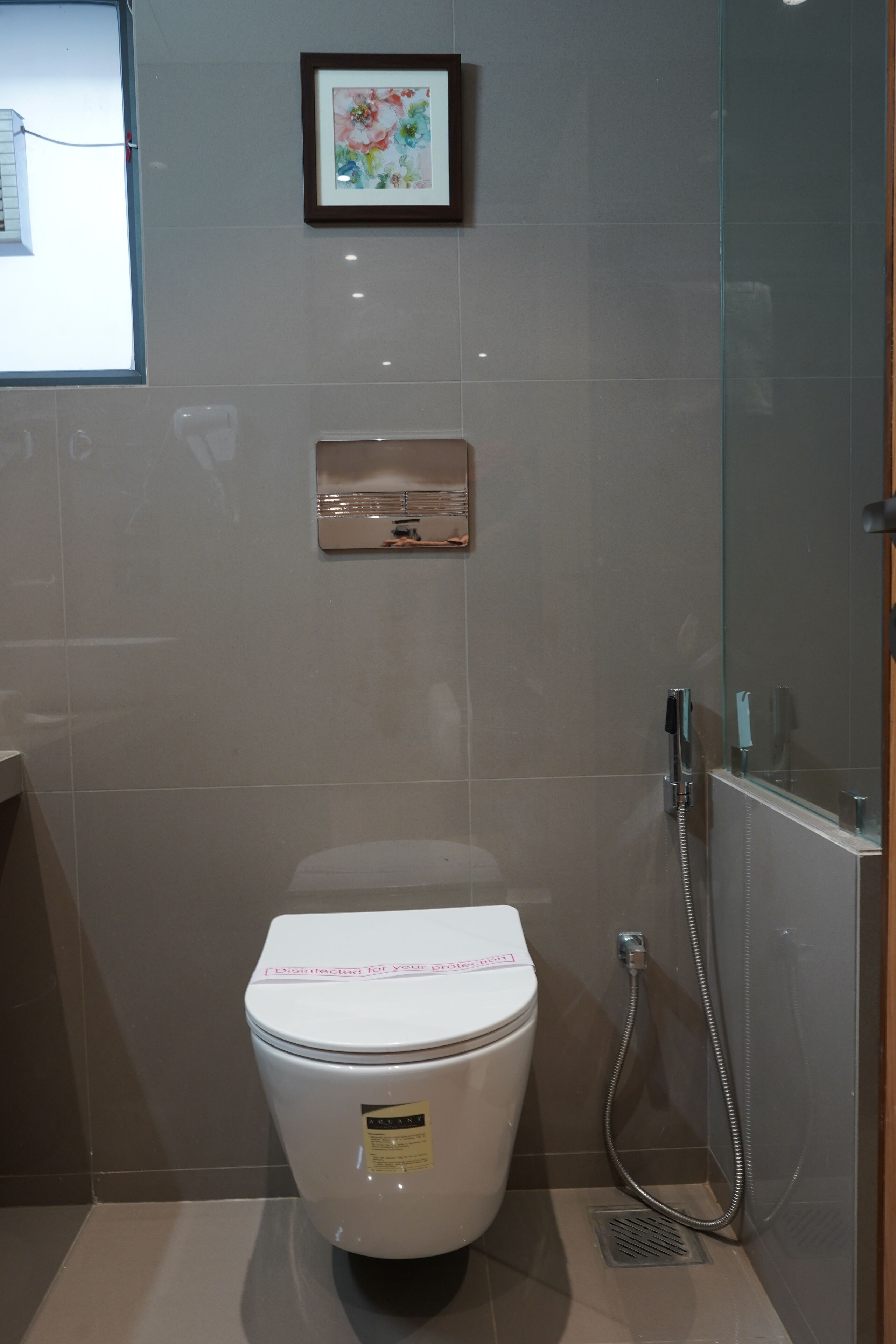 Une salle de bain moderne avec des toilettes, une œuvre d’art florale encadrée au mur et une cabine de douche en verre.