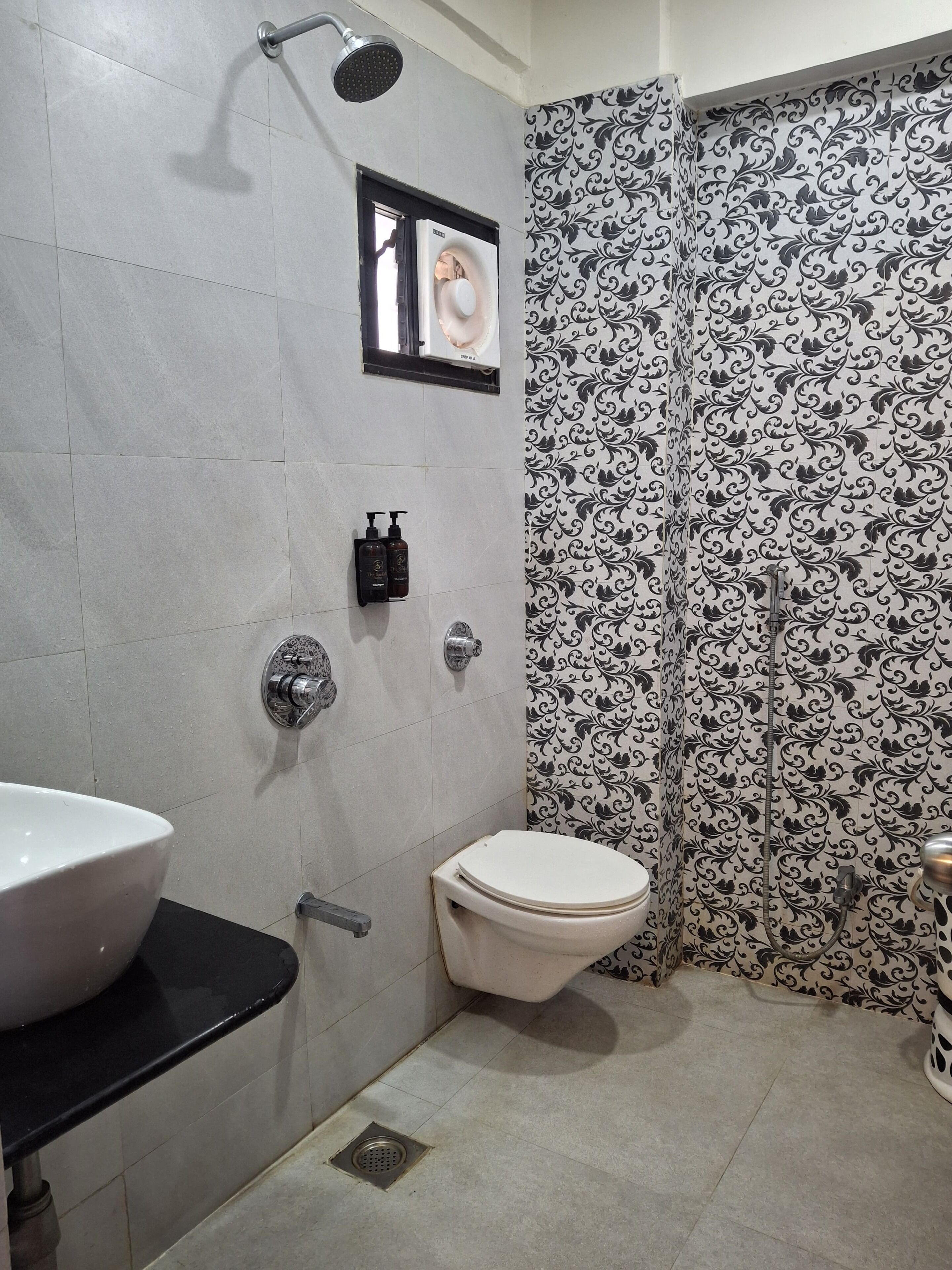 A bathroom with a white sink, toilet, and shower. There are two bottles of shampoo and conditioner on the wall.